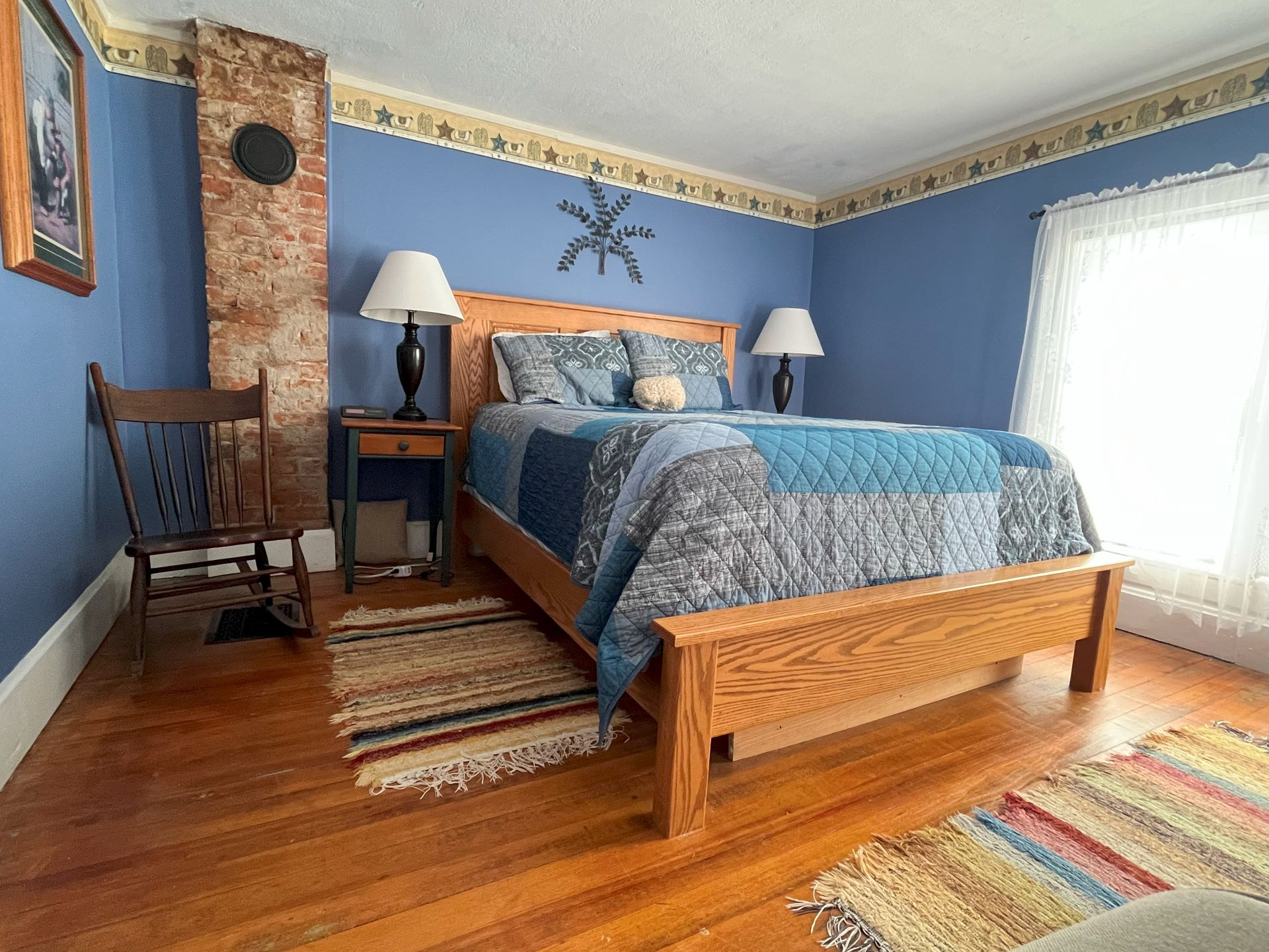 A cozy bedroom with blue walls, a patchwork quilt on a wooden bed, and a brick pillar in the corner.