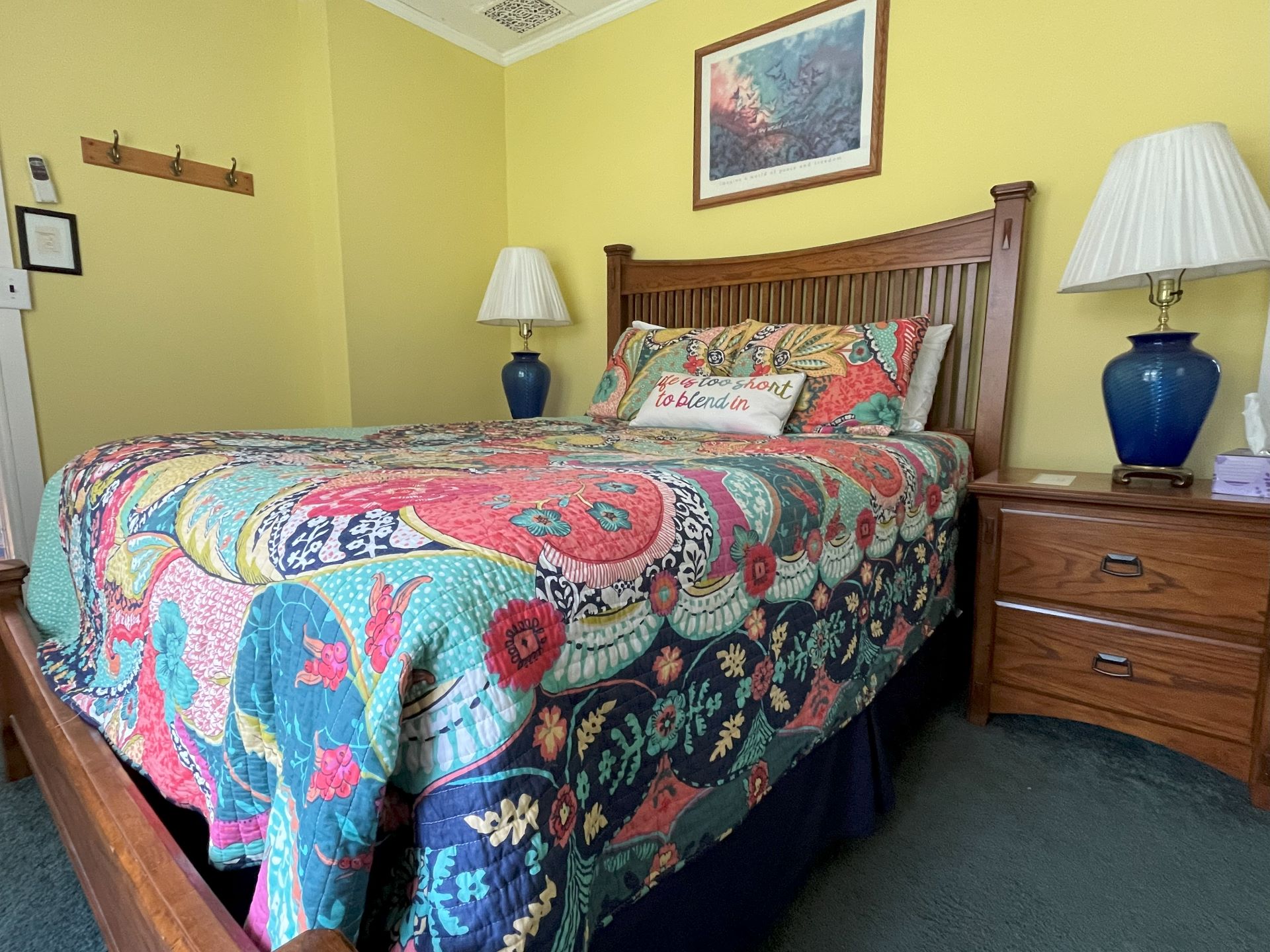A cozy bedroom with bright yellow walls, a colorful floral and paisley quilt, and dark wood furniture.