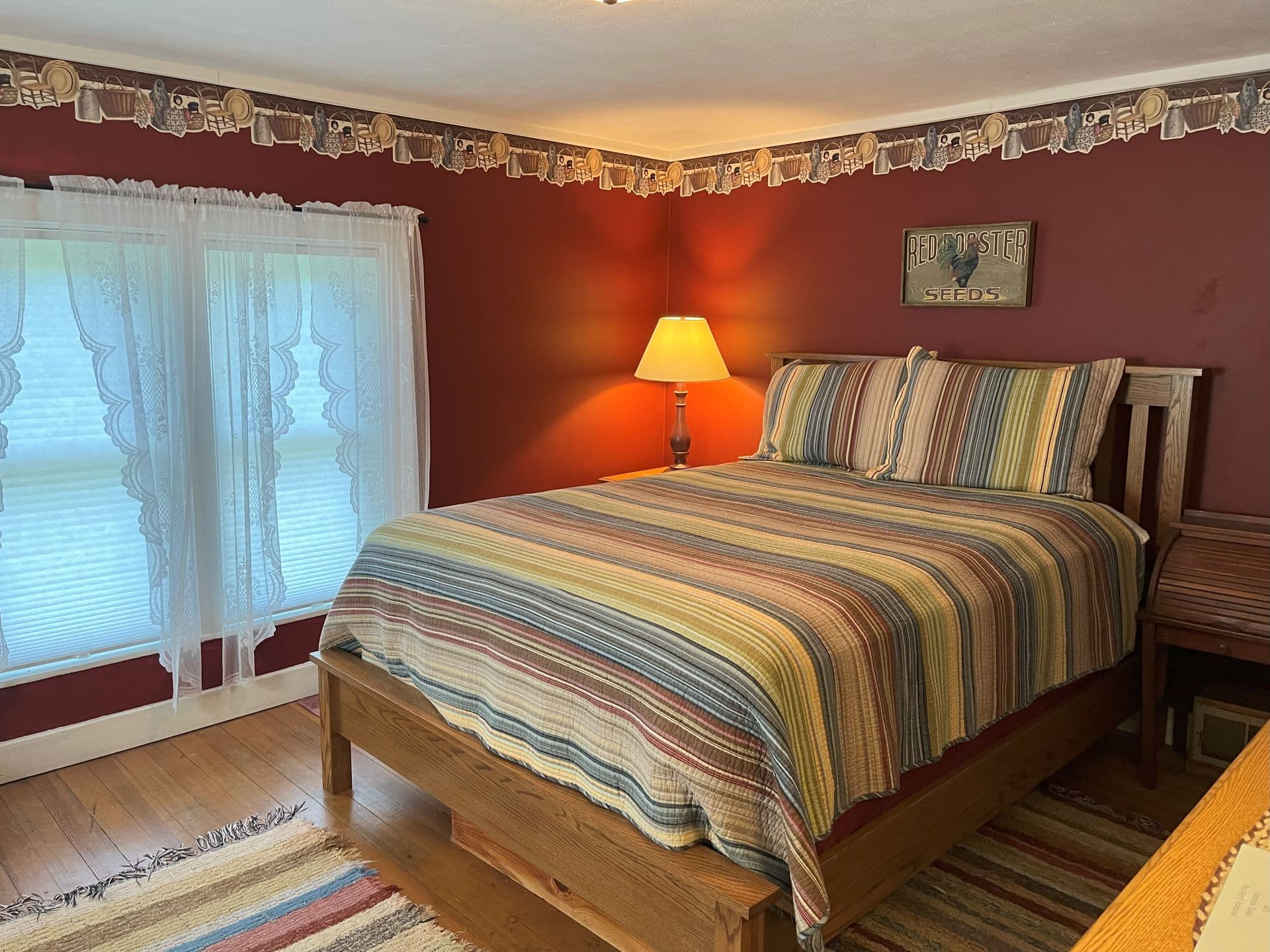 A rustic bedroom with burgundy walls, a striped quilt, and a wooden bed frame.