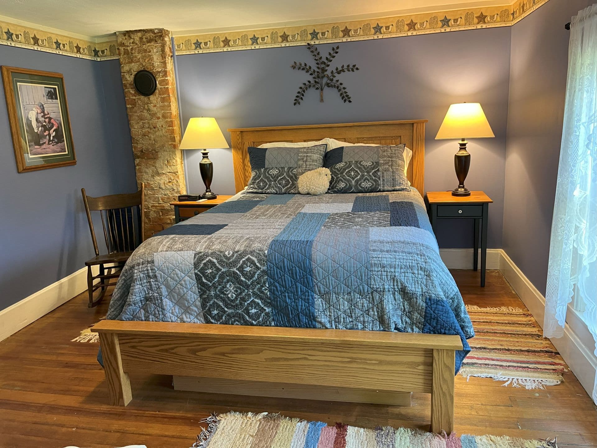 A rustic bedroom with light purple walls, a patchwork quilt in shades of blue and gray, and a wooden bed frame.