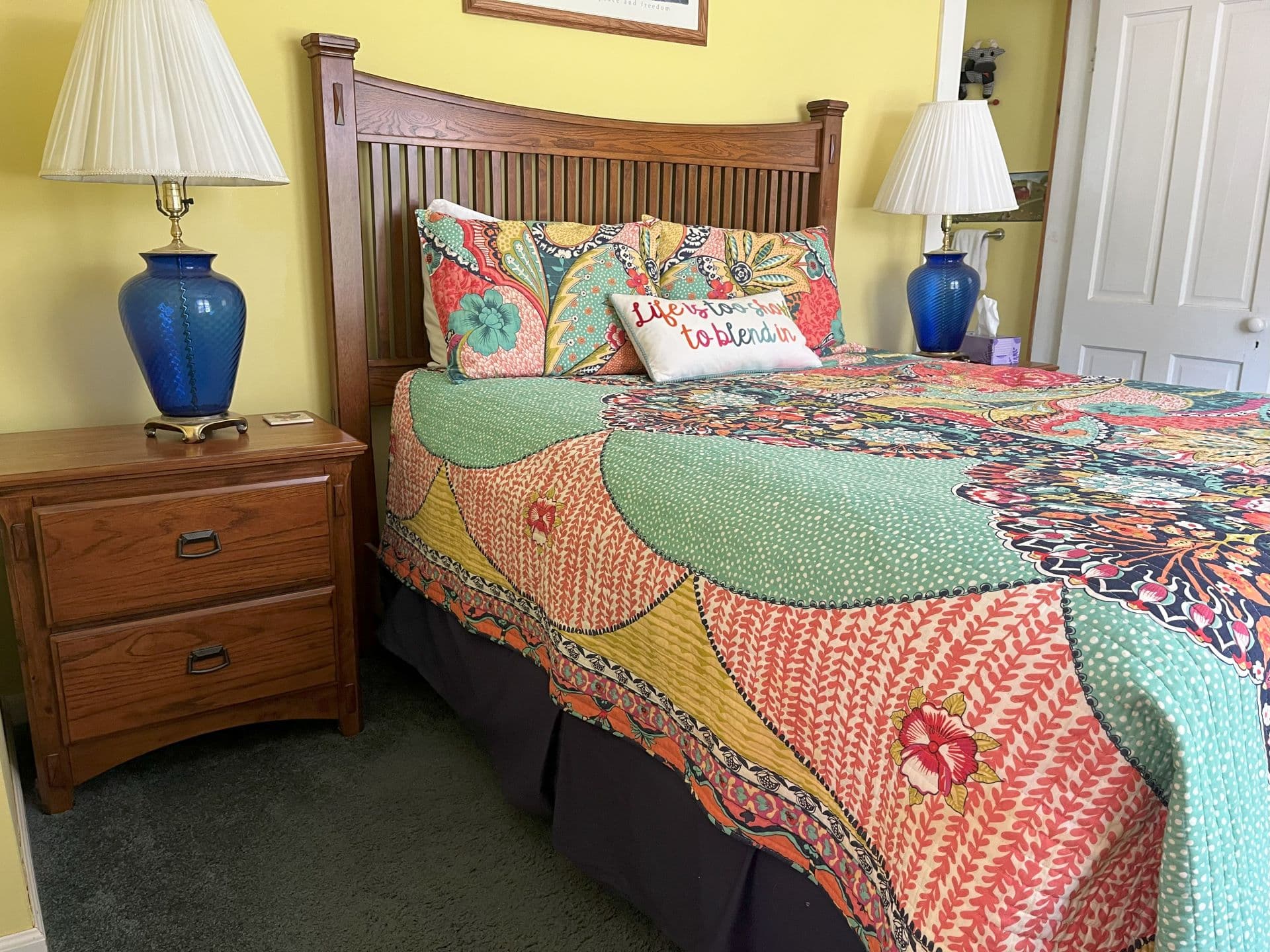 A vibrant bedroom with yellow walls, a multi-colored floral quilt, and a wooden bed with a headboard.
