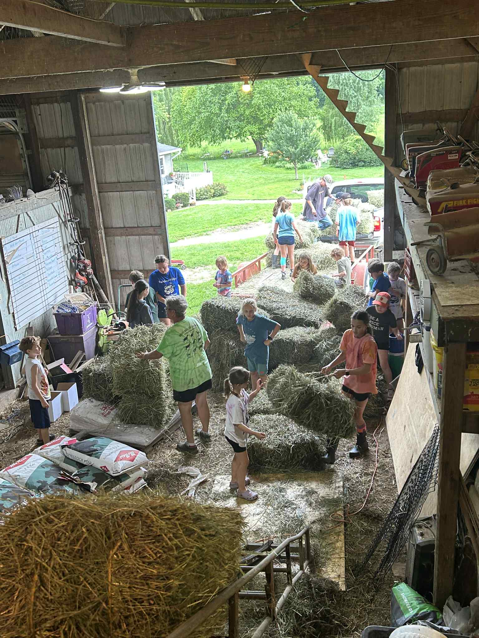 A group of children and adults are working together to stack bales of hay inside a barn.