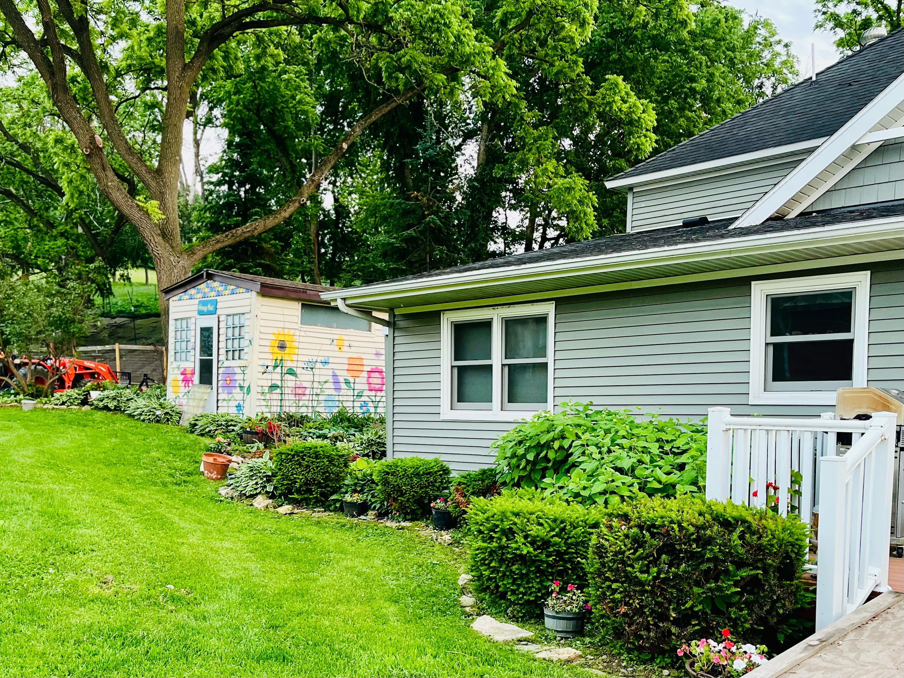 A well-maintained yard features a colorful garden shed and lush greenery near a house with a deck.