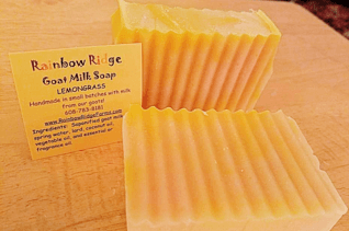 A close-up of two bars of lemon grass goat milk soap beside a business card on a wooden surface.